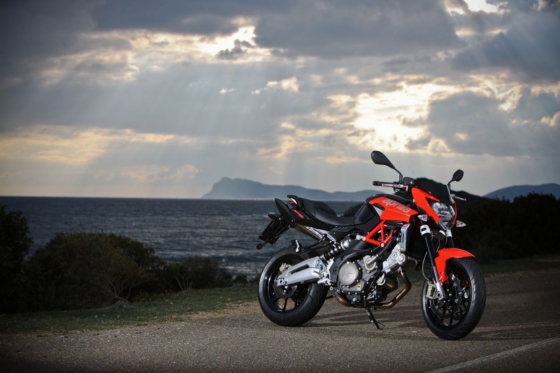 black and orange sports bike parked on gray concrete road near body of water during daytime