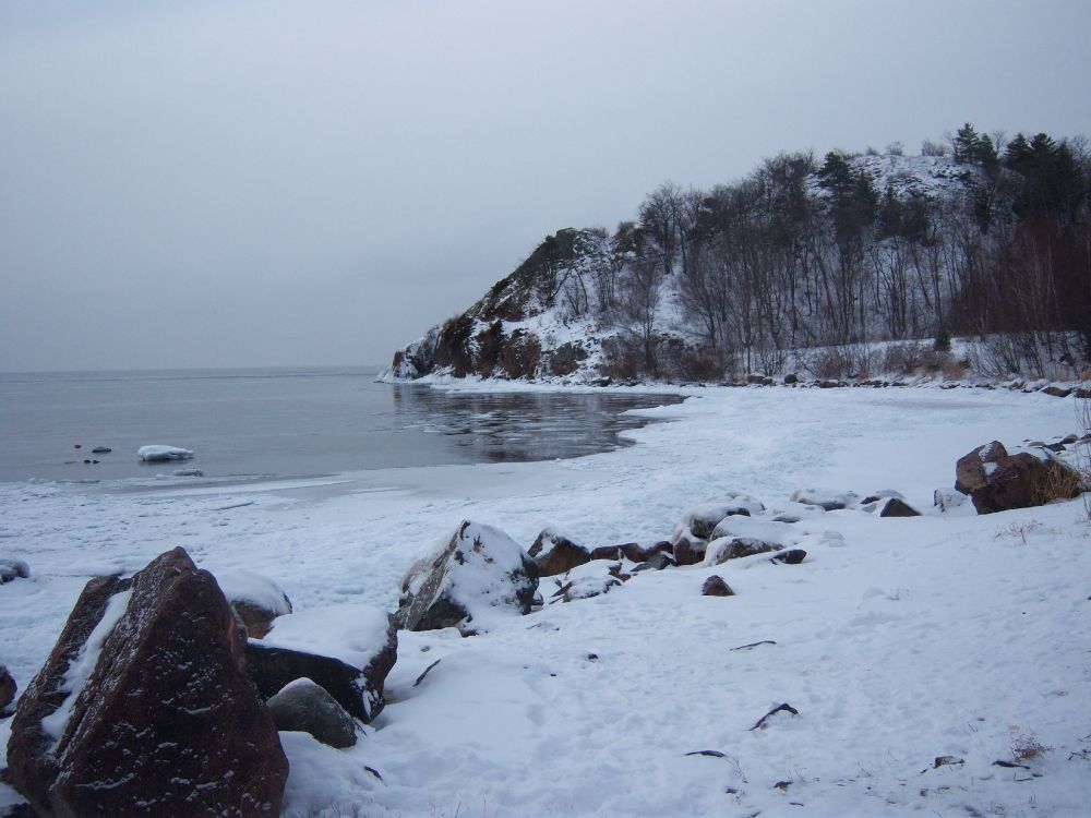 snow covered rocks by the sea during daytime