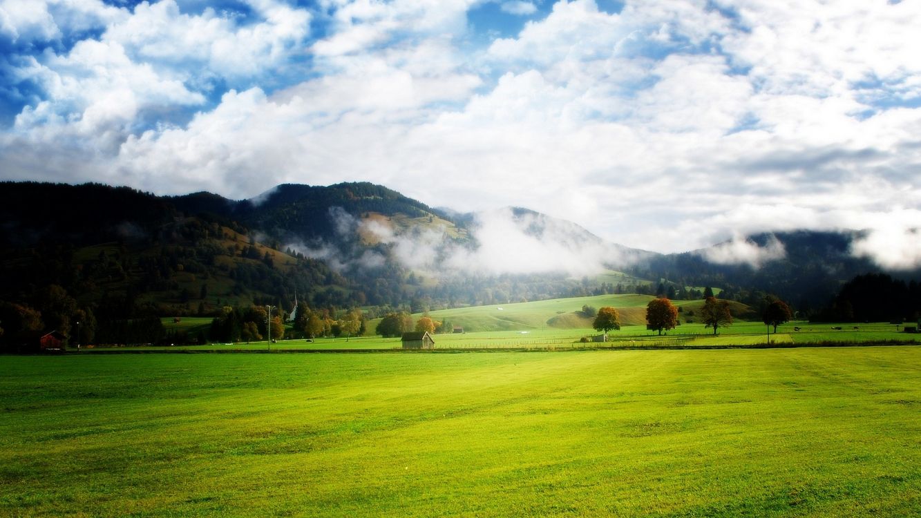 green grass field near mountain under white clouds during daytime