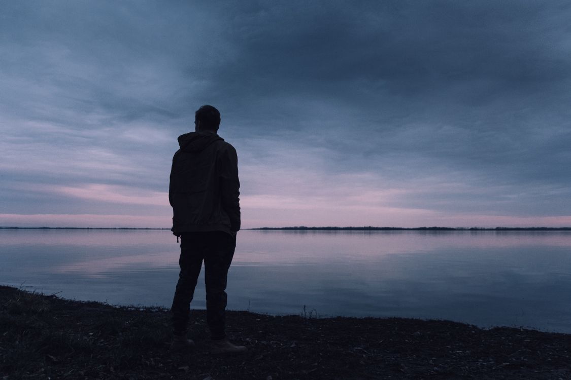 man in black jacket standing near body of water during daytime