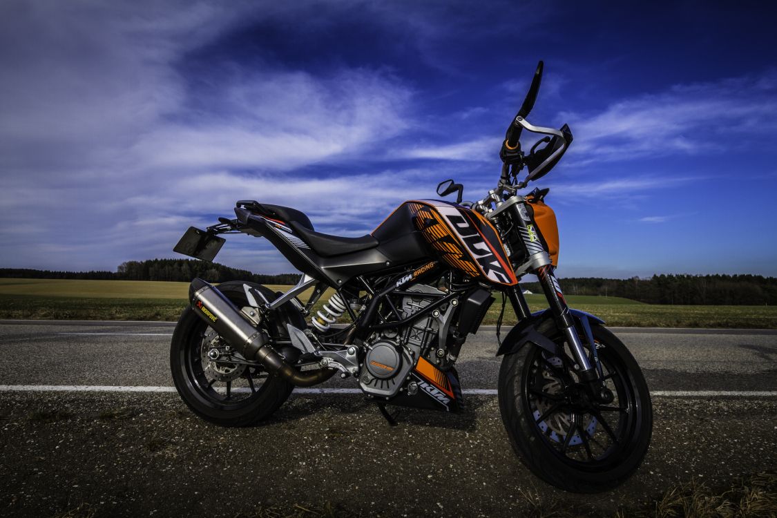 Orange and Black Motorcycle on Black Asphalt Road Under Gray Cloudy Sky. Wallpaper in 5184x3456 Resolution
