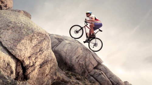 Image man in white shirt and black shorts riding on black mountain bike on brown rock mountain