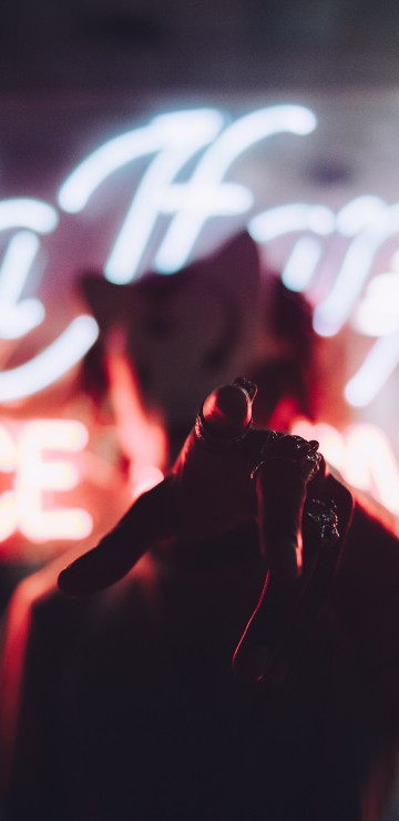 Image person in red jacket standing in front of red and white neon light signage