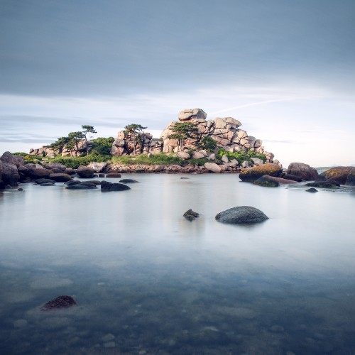 Image green and brown rock formation on body of water under blue sky during daytime