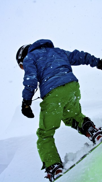 Image person in blue jacket and green pants riding on ski blades on snow covered ground during