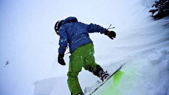 Image person in blue jacket and green pants riding on ski blades on snow covered ground during