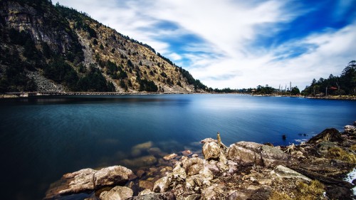 Image person sitting on rock near body of water during daytime