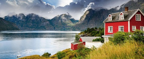 Image red and white wooden house near lake and mountains under blue sky during daytime