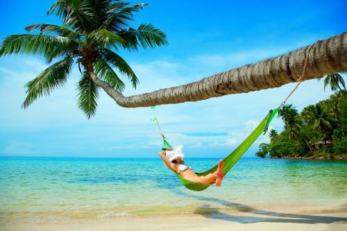 Image woman in white shirt and green shorts lying on hammock under coconut tree during daytime