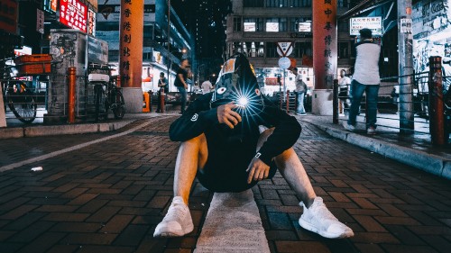 Image man in black and white nike backpack sitting on sidewalk during daytime