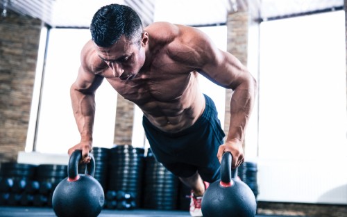 Image man in black tank top and black shorts holding black kettle bell