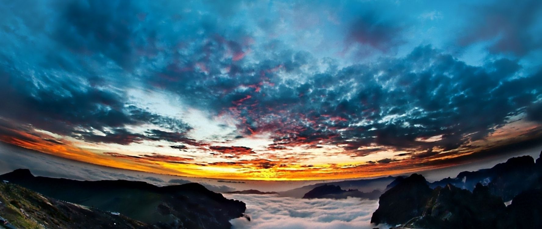 silhouette of person standing on rock formation under blue and white cloudy sky during daytime