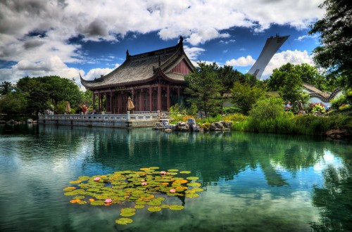 Image brown and white house near green trees and lake under blue sky and white clouds during