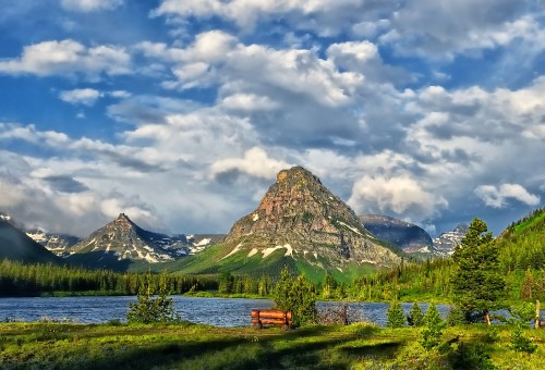 Image brown wooden bench on green grass field near lake and mountain under white clouds and blue