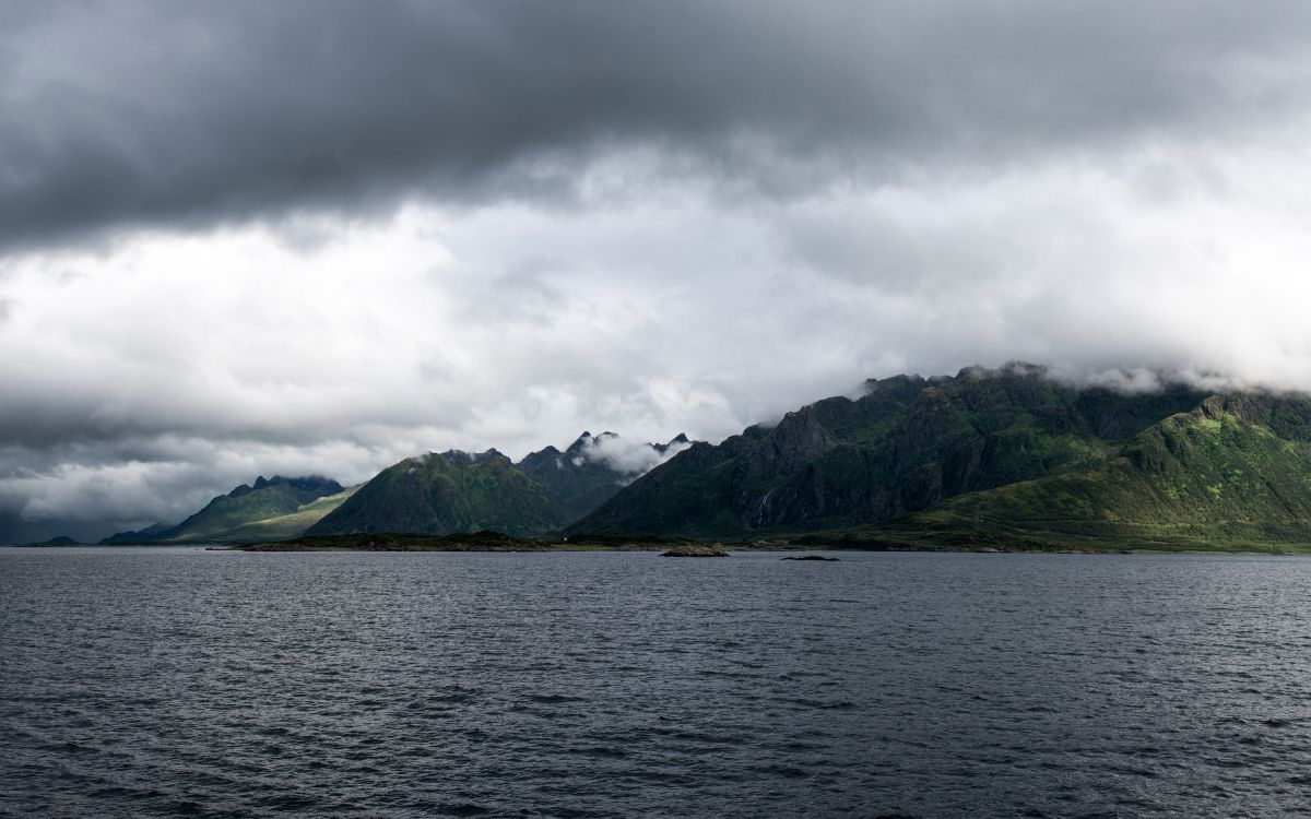 green mountain beside body of water under cloudy sky during daytime