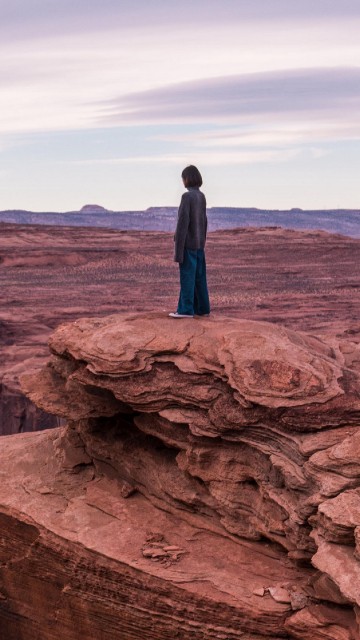 Image man in blue jacket standing on brown rock formation during daytime
