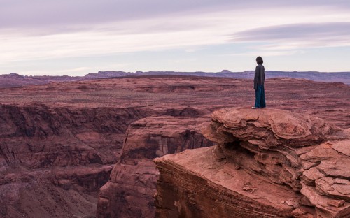 Image man in blue jacket standing on brown rock formation during daytime