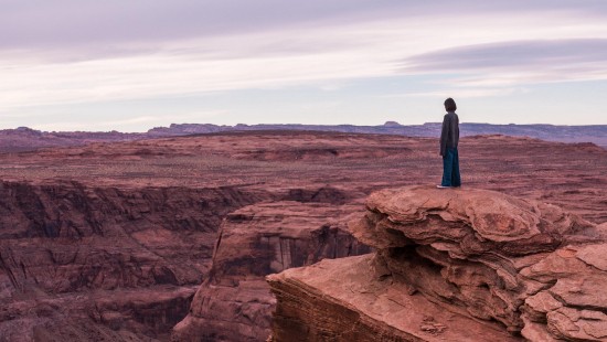 Image man in blue jacket standing on brown rock formation during daytime