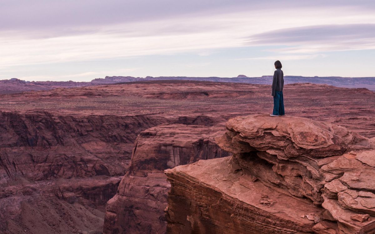 man in blue jacket standing on brown rock formation during daytime