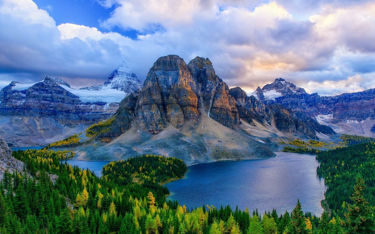 green trees near body of water and mountain under white clouds and blue sky during daytime