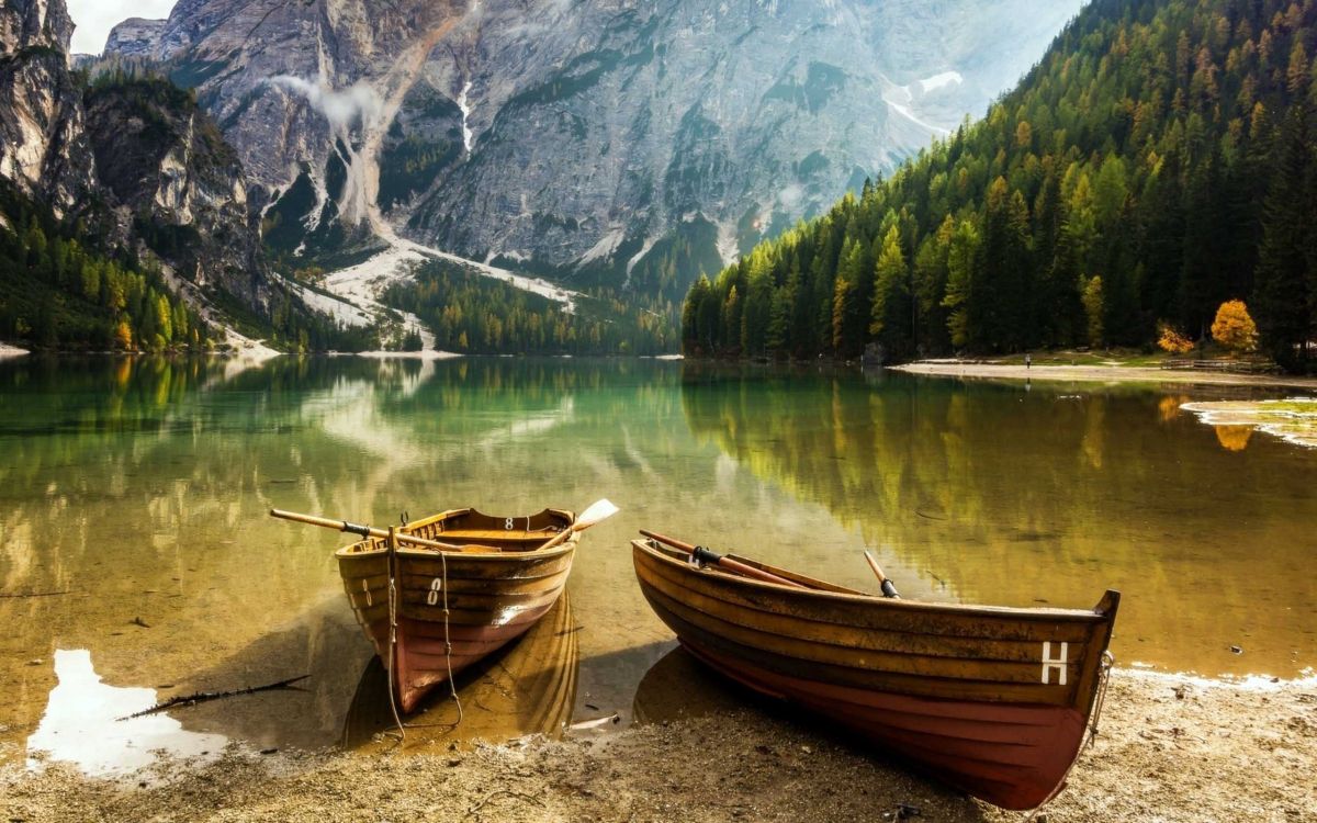 brown boat on shore near green trees and mountain during daytime