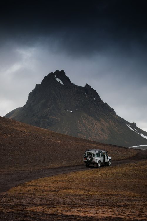 white suv on brown field near mountain under white sky during daytime