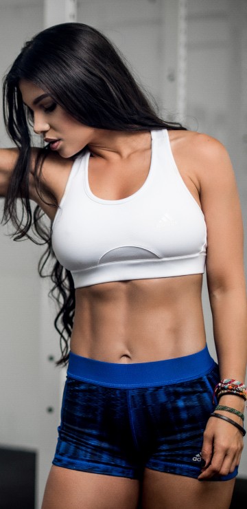Image woman in white sports bra and blue shorts holding black barbell