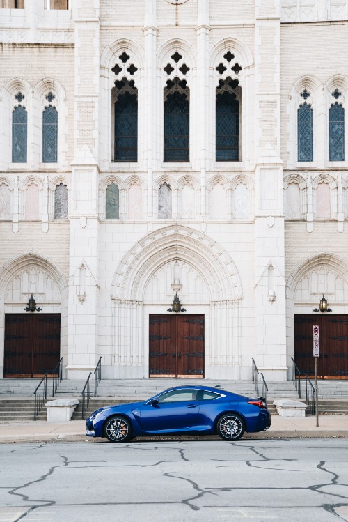 Image blue coupe parked beside white concrete building during daytime