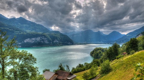 Image brown wooden house near green trees and body of water under cloudy sky during daytime