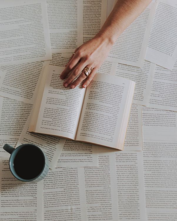 person holding white ceramic mug on white book page