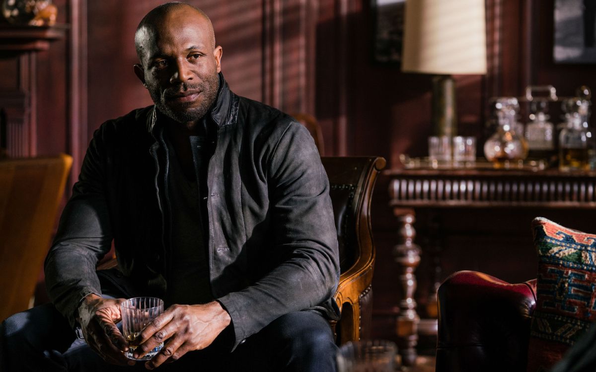 Mann in Schwarzem Hemd Und Blauer Jeans Sitzt Auf Braunem Holzsessel. Wallpaper in 3840x2400 Resolution