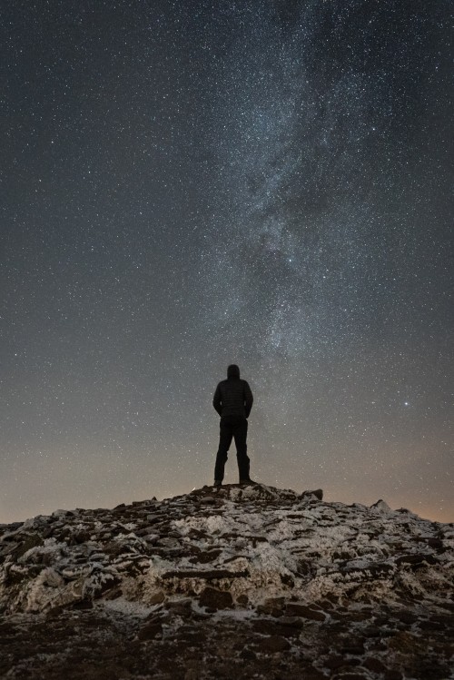 Image silhouette of man standing on rocky hill under starry night