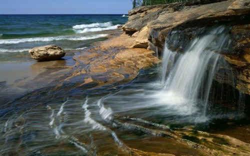 Image water falls on brown rocky shore during daytime