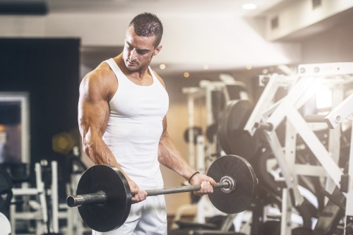 Image man in white tank top carrying barbell