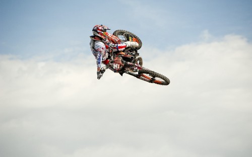 Image man riding motocross dirt bike doing stunts under white clouds during daytime