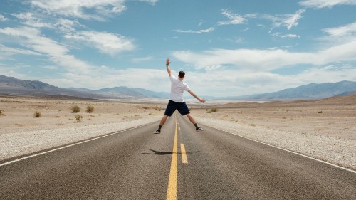 Image man in white t-shirt and black shorts running on gray asphalt road under blue and