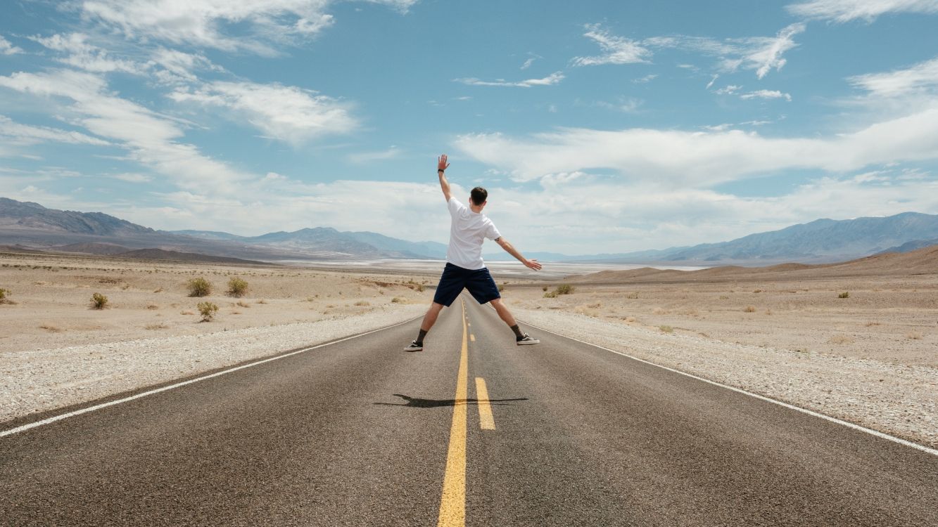 man in white t-shirt and black shorts running on gray asphalt road under blue and