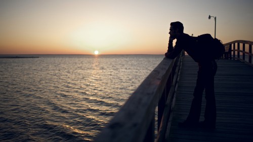 Image man in black jacket standing on dock during sunset