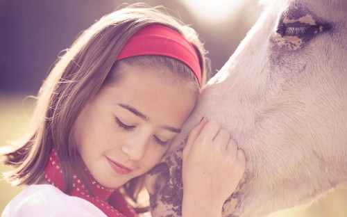 Image woman in red and white knit cap kissing white short coated dog