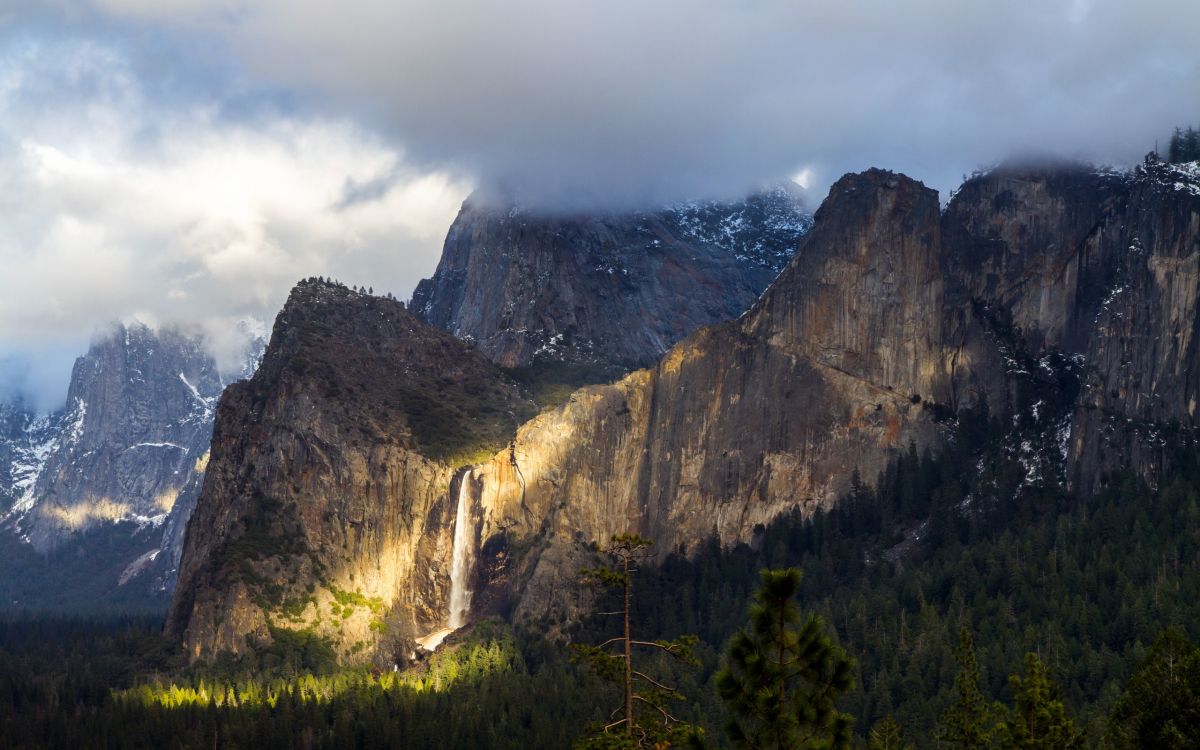 green trees near brown mountain under white clouds during daytime