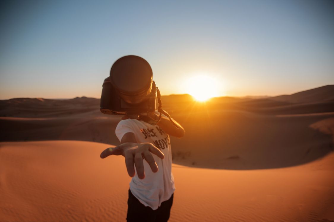 man in white shirt and black pants standing on sand during sunset