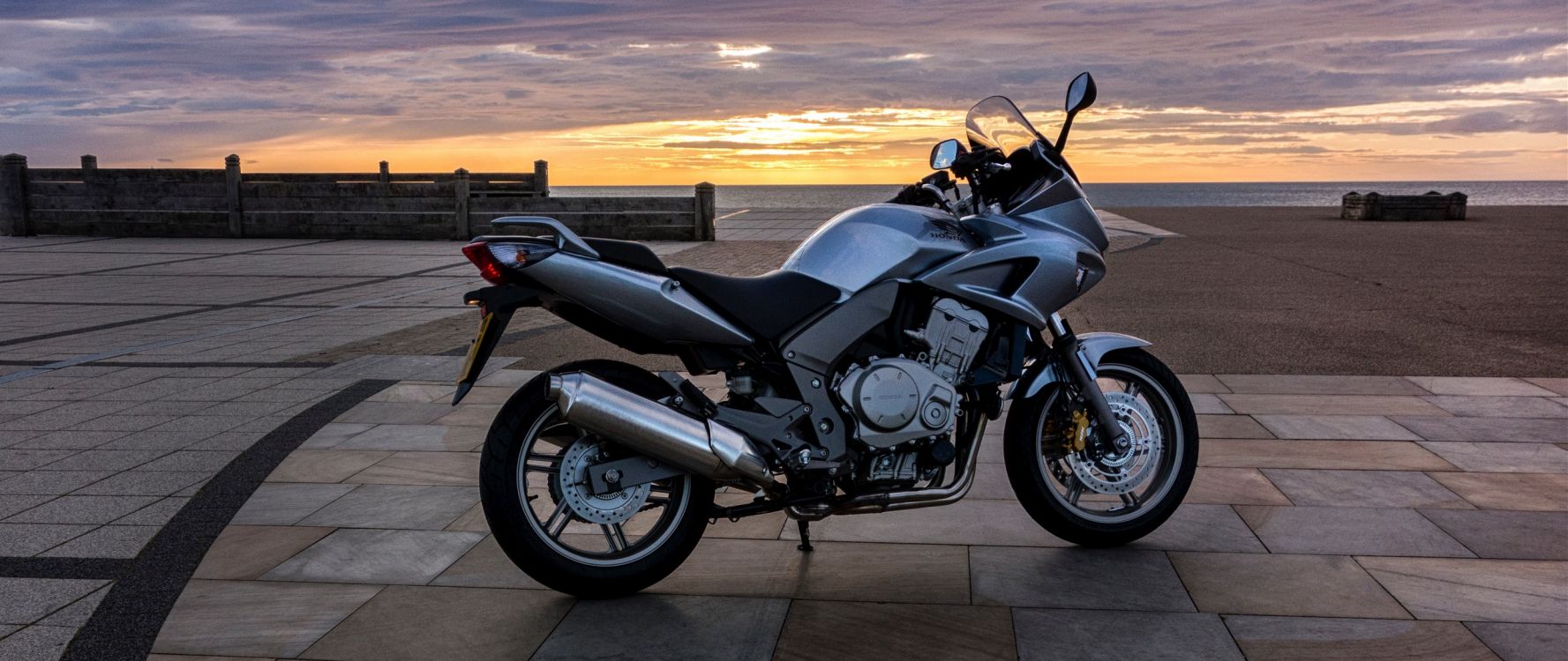 Schwarz-silbernes Cruiser-Motorrad Auf Grauer Betonstraße Bei Sonnenuntergang. Wallpaper in 2560x1080 Resolution