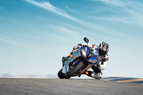 Image man in blue and white sports bike suit riding on blue sports bike on gray asphalt