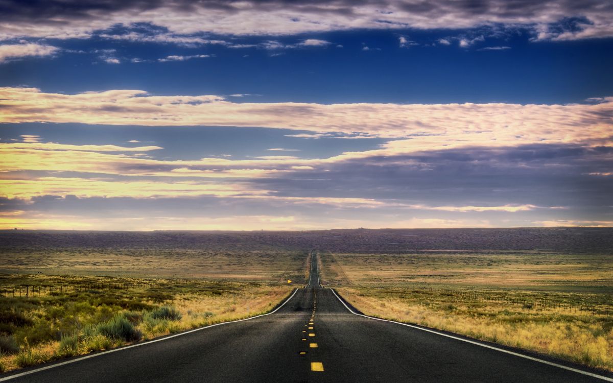 black asphalt road between green grass field under blue and white sunny cloudy sky during daytime