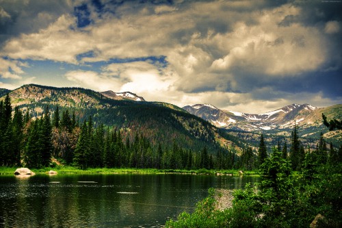 Image lake surrounded by trees and mountains under cloudy sky during daytime