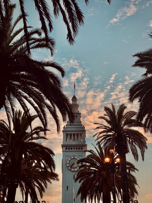 Image white concrete tower with clock under blue sky and white clouds during daytime