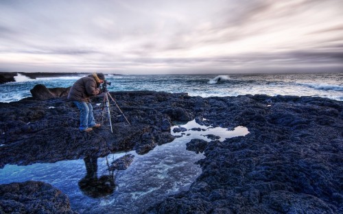 Image man in blue jacket and black pants standing on rocky shore