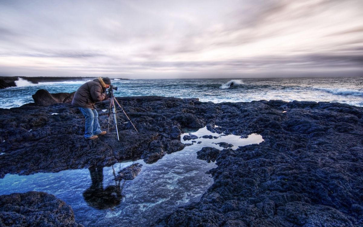 man in blue jacket and black pants standing on rocky shore