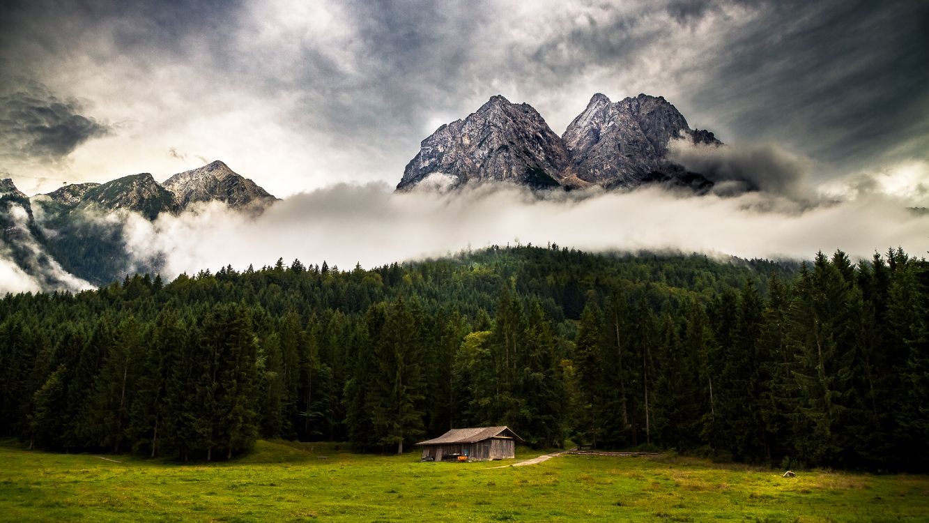 brown wooden house on green grass field near green trees and mountain under white clouds during