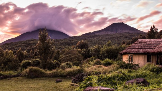 Image brown wooden house on green grass field near mountain under white clouds during daytime